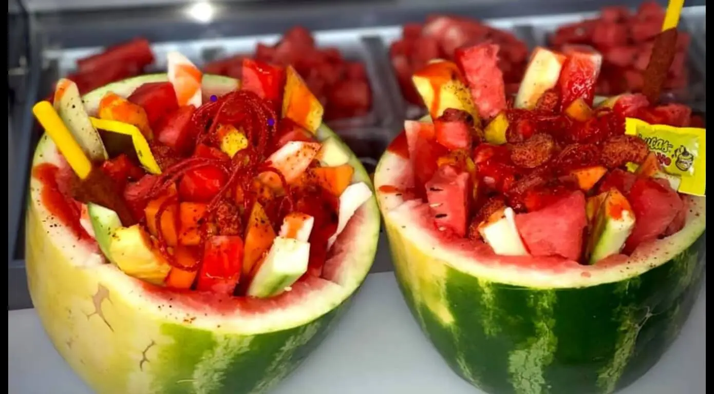 A halved watermelon filled with an assortment of fruits, candies, and drizzled sauces, showcasing the colorful and festive Sandia Loca."